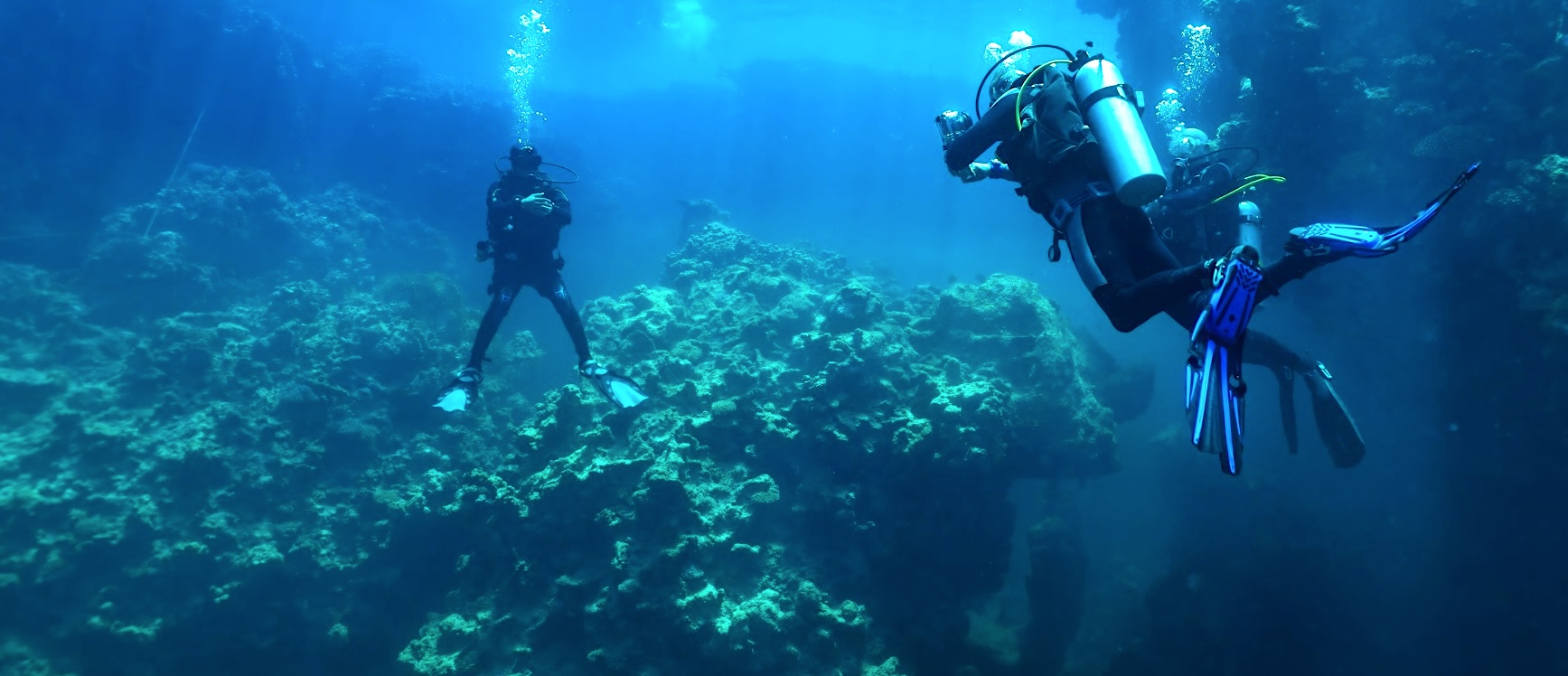 Scuba divers swimming through a sunlit underwater cave